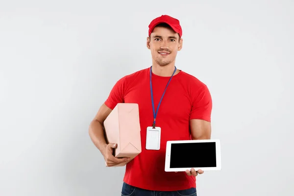 Happy young courier with tablet and parcel on white background — Stok Foto