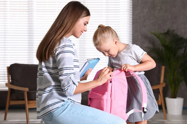 젊은 어머니와 어린 아이가 집에서 학교 가방에 교과서를 넣어 — 스톡 사진