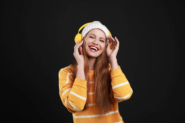 Mladá žena naslouchající hudbě se sluchátky na černém pozadí — Stock fotografie