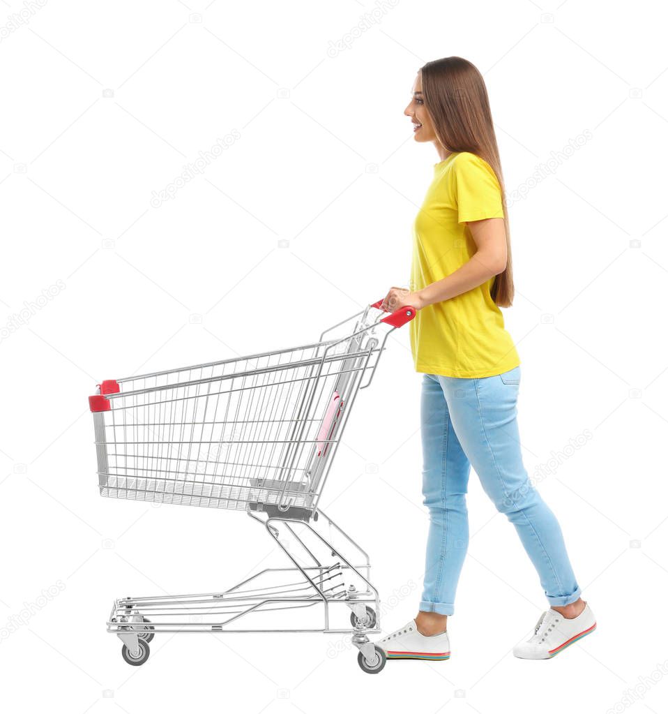 Young woman with empty shopping cart on white background