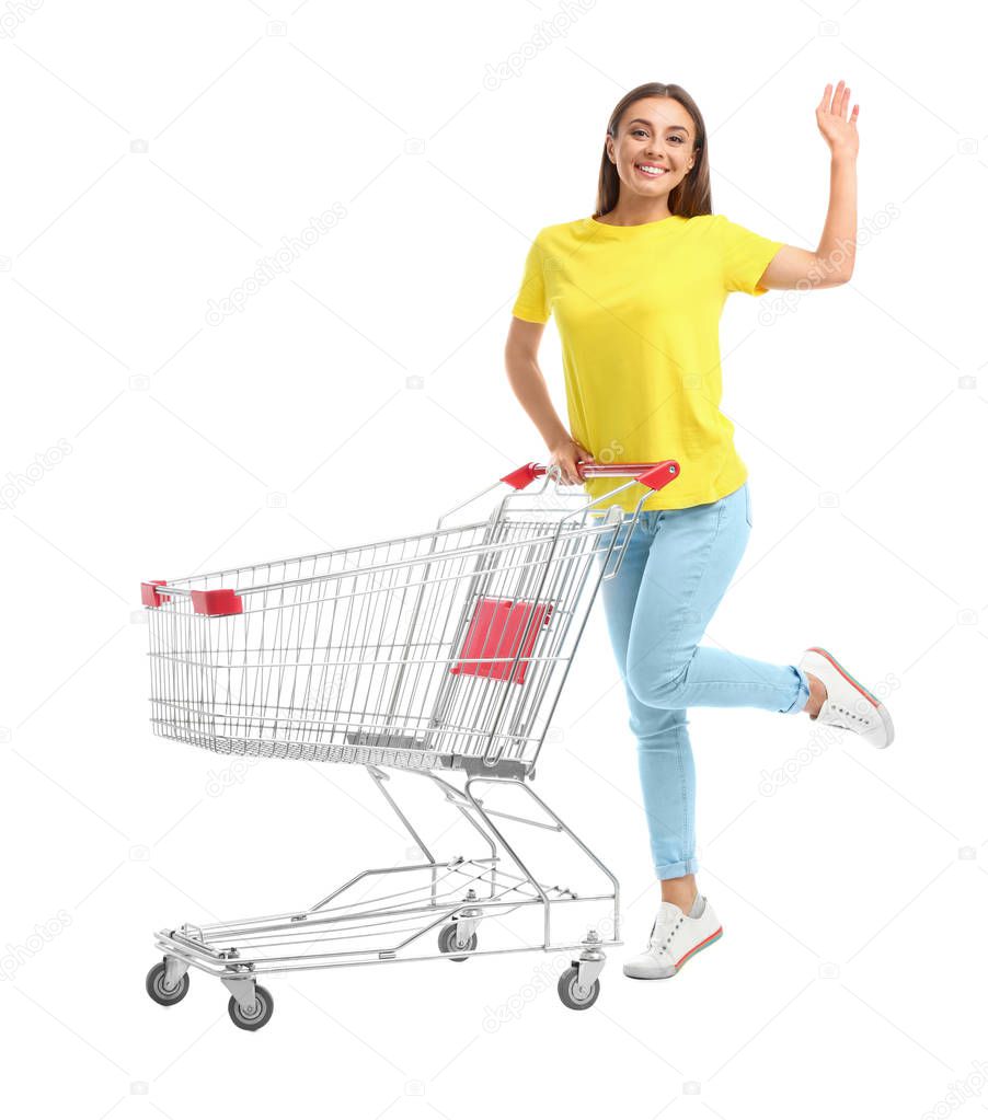 Young woman with empty shopping cart on white background