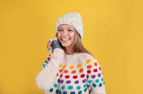 Mujer joven en suéter cálido, manoplas y sombrero sobre fondo amarillo. Temporada de invierno — Foto de Stock