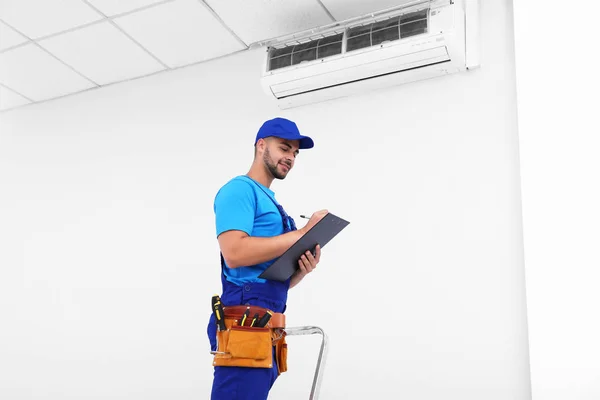 Técnico profissional com prancheta perto de ar condicionado moderno dentro de casa — Fotografia de Stock