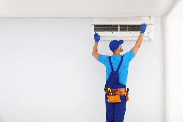 Professional technician maintaining modern air conditioner indoors. Space for text — Stock Photo, Image