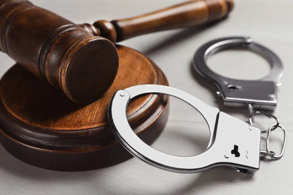 Молоток судьи и наручники на белом деревянном фоне, крупным планом. Уголовное право — стоковое фото