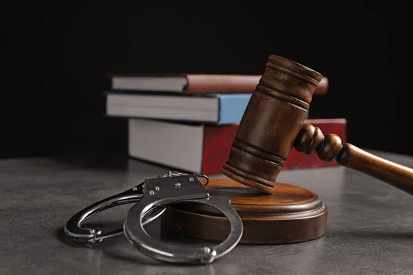 Судья молоток, наручники и книги на сером столе на черном фоне. Уголовное право — стоковое фото