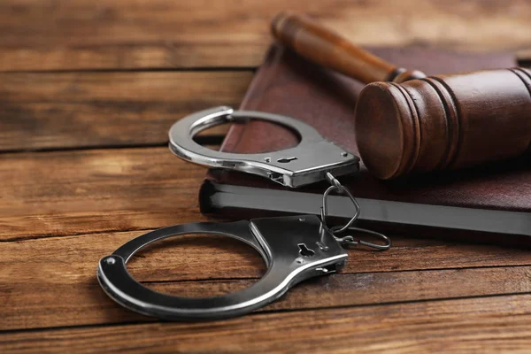 Молоток, наручники и книга на деревянном столе, крупным планом. Уголовное право — стоковое фото