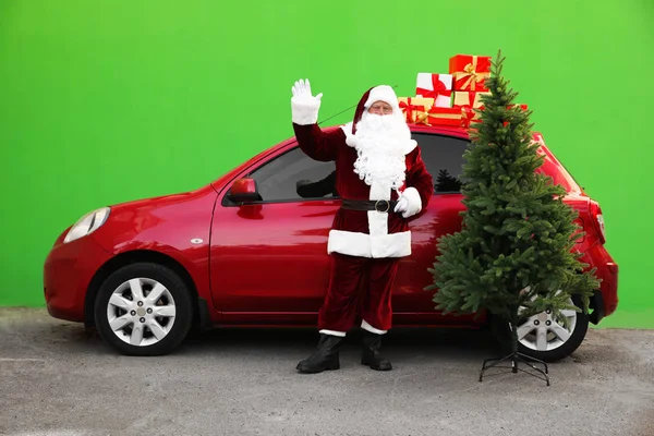 Autentyczny Święty Mikołaj w pobliżu samochodu z jodłami i prezentuje zielone tło — Zdjęcie stockowe