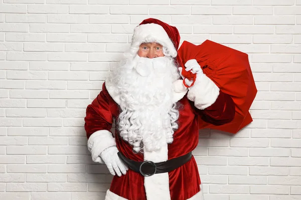 Papai Noel autêntico com saco cheio de presentes contra parede de tijolo branco — Fotografia de Stock