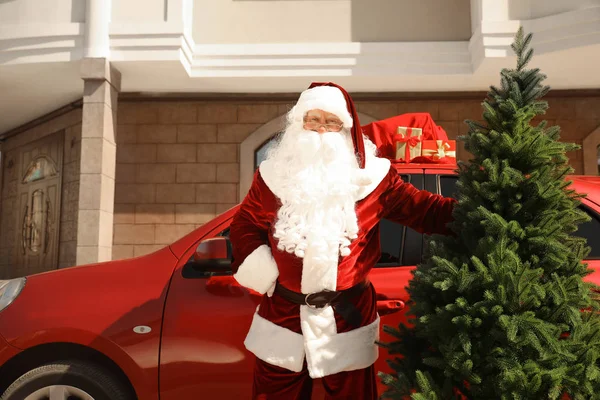 Autentyczny Święty Mikołaj w pobliżu samochodu z jodełką i torbą pełną prezentów na zewnątrz — Zdjęcie stockowe