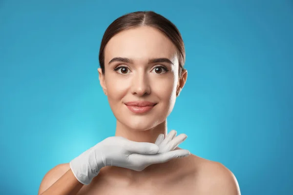 Médico examinando o rosto da mulher antes da cirurgia plástica em fundo azul claro — Fotografia de Stock