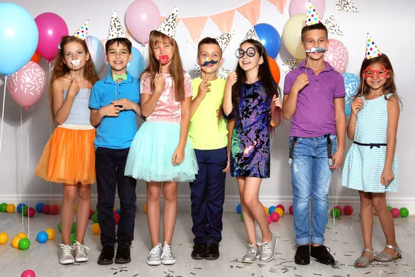 Niños felices con accesorios de cabina de fotos en la fiesta de cumpleaños en el interior — Foto de Stock