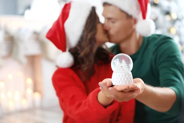 Casal feliz em casa, foco em mãos com globo de neve — Fotografia de Stock