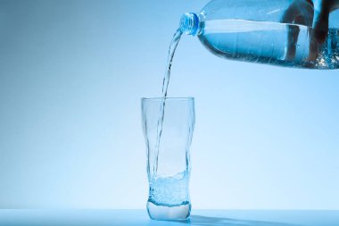 Mavi arka plana karşı şişeden cama su dökmek. Ferahlatıcı içecek