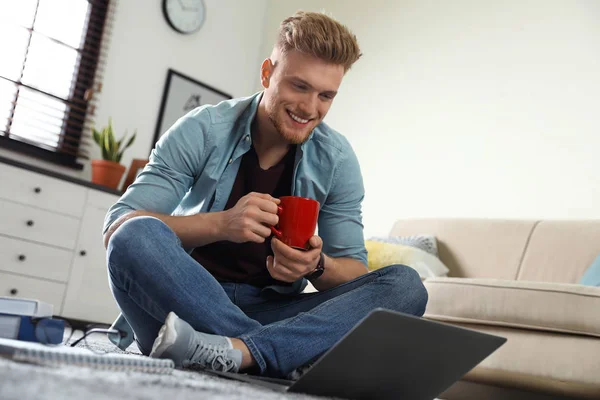 Young man using laptop while sitting on floor in living room — Stock Photo, Image