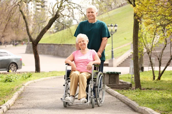 Ανώτερη γυναίκα σε αναπηρικό αμαξίδιο και ώριμο άντρα την ηλιόλουστη μέρα σε εξωτερικούς χώρους — Φωτογραφία Αρχείου