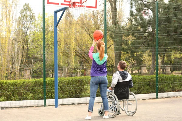 Мужчина в инвалидной коляске и молодая женщина играют в баскетбол на спортивной площадке — стоковое фото
