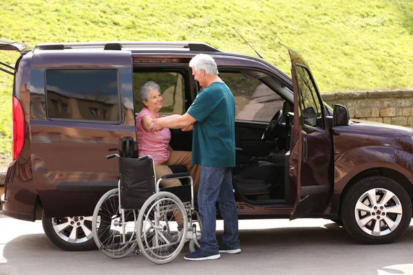 Dojrzały mężczyzna pomagając starszy kobieta do wyjść z Van na wózku inwalidzkim na zewnątrz — Zdjęcie stockowe