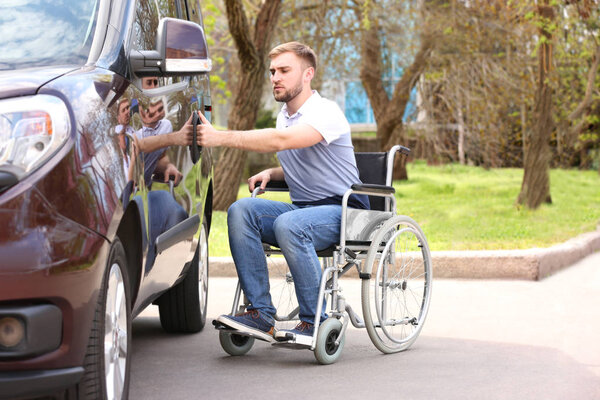 Young man in wheelchair opening door of his van outdoors