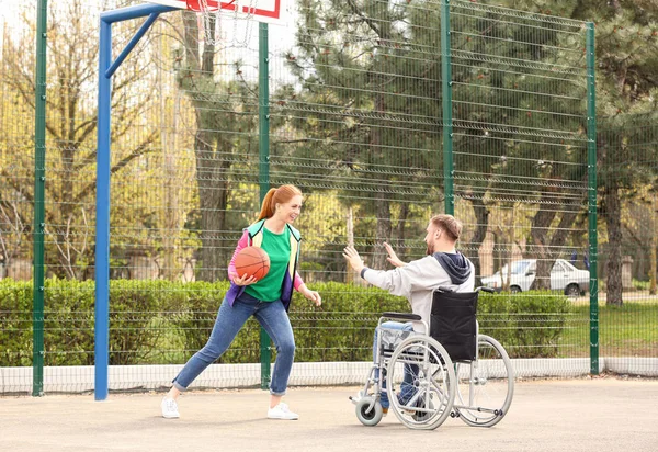Człowiek na wózku inwalidzkim i młodej kobiecie grając w koszykówkę na ziemi sportowej — Zdjęcie stockowe
