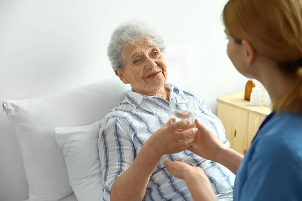 Krankenschwester gibt älteren Frauen im Haus ein Glas Wasser. Medizinische Hilfe — Stockfoto