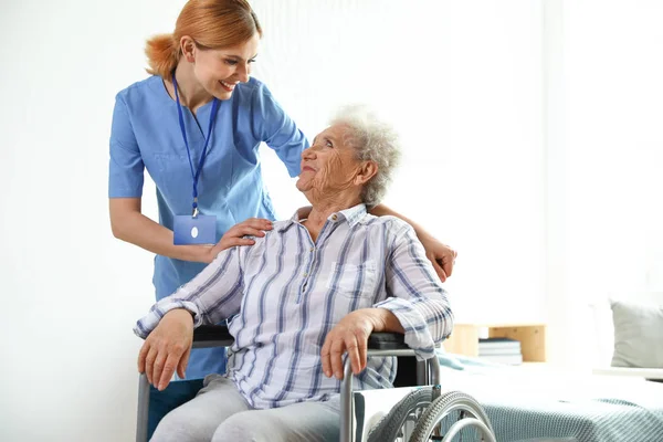 Enfermera asistiendo a anciana en silla de ruedas en interiores — Foto de Stock