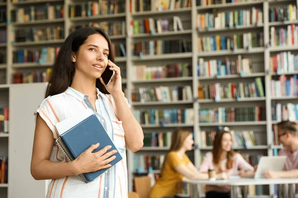 Fiatal nő könyveket beszél telefonon a könyvtárban. Szóköz a szöveghez — Stock Fotó
