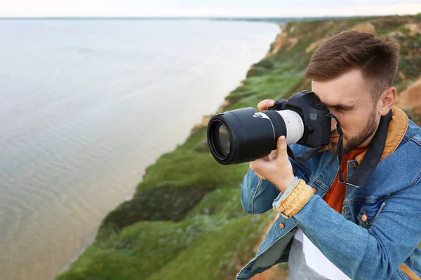 Чоловік фотограф фотографує красивий пейзаж з професійною камерою на зеленому пагорбі. Простір для тексту — стокове фото