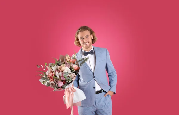Jonge knappe man in stijlvolle pak met mooie bloem boeket op roze achtergrond — Stockfoto