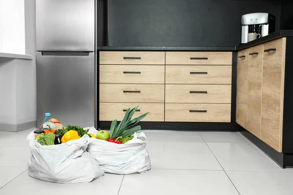 Πλαστικές σακούλες με λαχανικά και άλλα προϊόντα στο πάτωμα στην κουζίνα. Χώρος για κείμενο — Φωτογραφία Αρχείου
