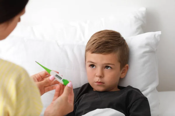 Mère mesurant la température de son fils malade au lit — Photo