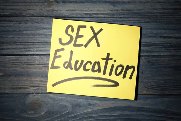 Nota con la frase "SEXO EDUCACIÓN" sobre fondo de madera oscura, vista superior — Foto de Stock