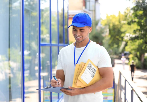 Joven mensajero con sobres acolchados y portapapeles al aire libre. Servicio de entrega — Foto de Stock