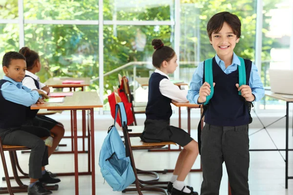 Menino vestindo uniforme escolar com mochila em sala de aula — Fotografia de Stock