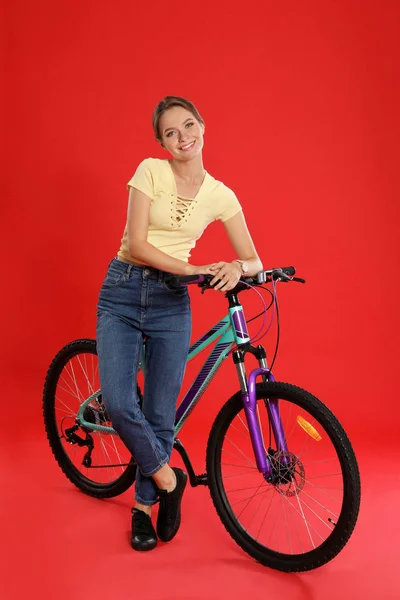 Mujer joven feliz con bicicleta sobre fondo rojo — Foto de Stock