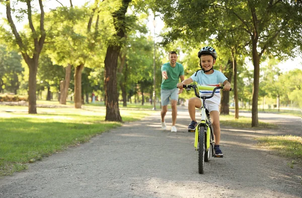 Père heureux apprenant à son fils à faire du vélo dans le parc — Photo