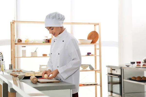 Female pastry chef preparing croissants at table in kitchen