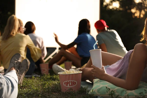 Young people with popcorn and drink watching movie in open air cinema, closeup — Stock Photo, Image