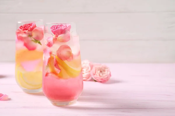 Deliziosa bevanda rinfrescante con limone e rose sul tavolo di legno rosa. Spazio per testo — Foto Stock