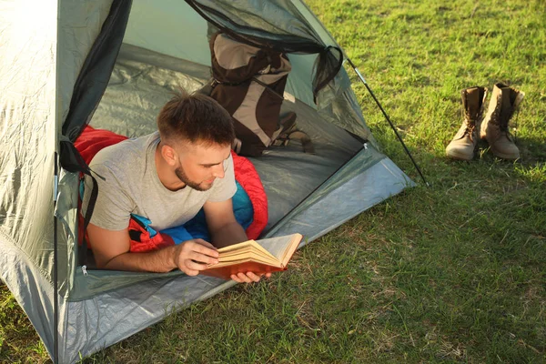 Junger Mann im Schlafsack mit Buch im Zelt — Stockfoto