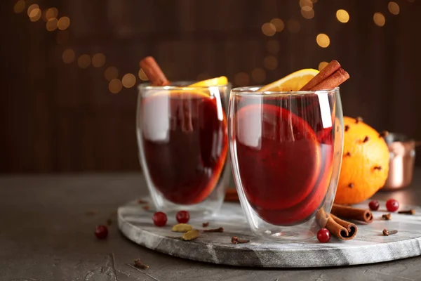 Verres de vin chaud savoureux sur table grise contre les lumières festives — Photo