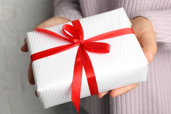 Young woman holding Christmas gift on light background, closeup — Stock Photo, Image