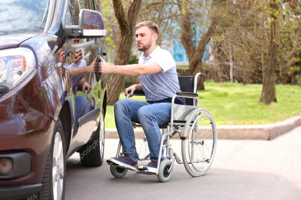 Young man in wheelchair opening door of his van outdoors