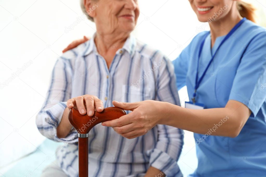 Nurse in uniform assisting elderly woman indoors, closeup