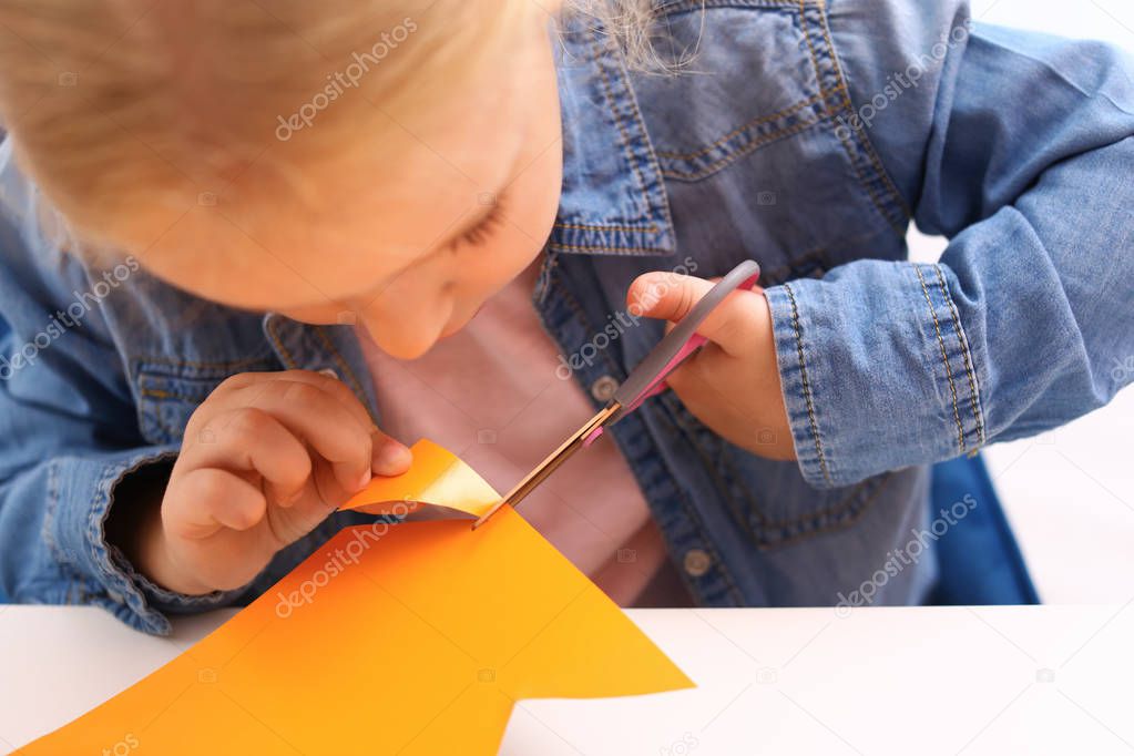 Little girl left-handed cutting construction paper at table, closeup