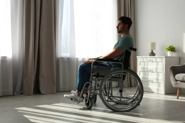 Молодой человек сидит в инвалидной коляске возле окна в помещении — стоковое фото