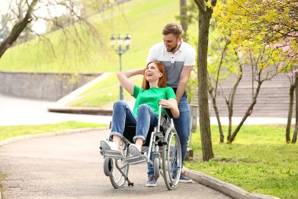 Happy woman in wheelchair and young man at park on sunny day