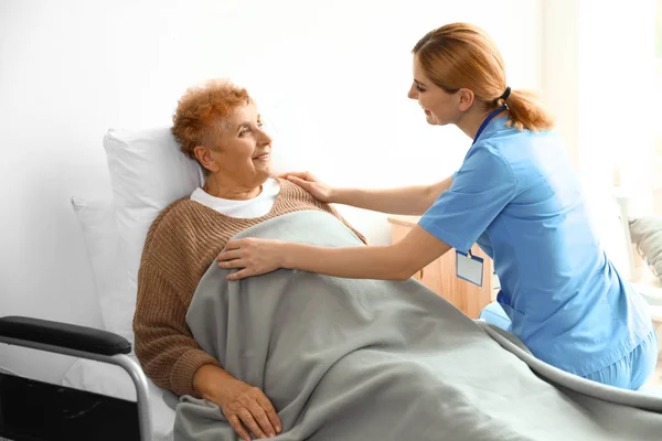 Enfermera en uniforme asistiendo a ancianas en interiores — Foto de Stock