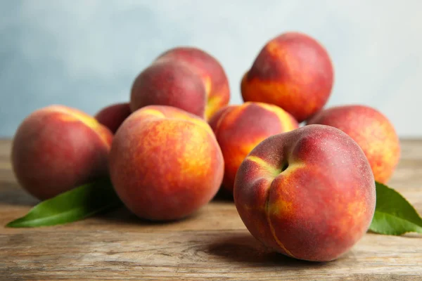 Fresh juicy peaches and leaves on wooden table against blue background