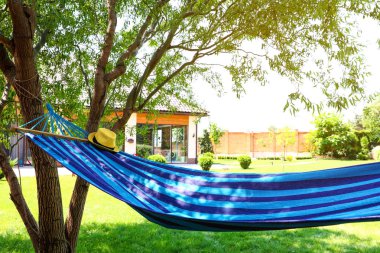 Güneşli bir günde açık havada şapkası ve kitabı olan rahat mavi bir hamak.